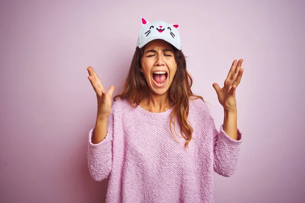 Young beautiful woman wearing funny cat cap standing over pink isolated background celebrating mad and crazy for success with arms raised and closed eyes screaming excited. Winner concept