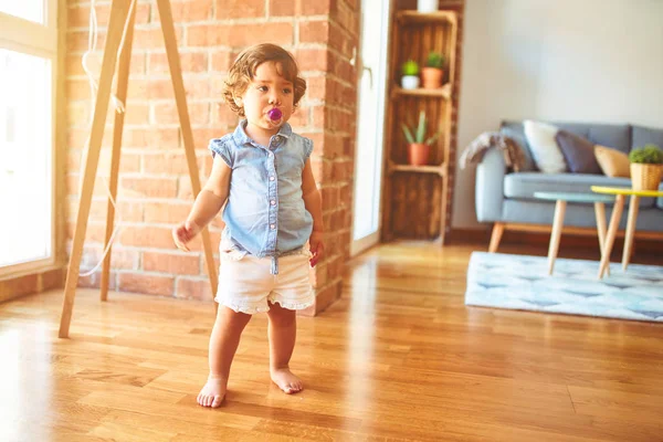 美丽的幼儿女孩穿着蓝色牛仔衬衫站在地板上使用奶嘴 — 图库照片