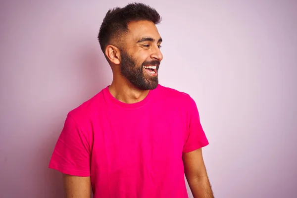 孤立したピンクの背景の上に立つTシャツを着た若いインド人男性が 笑顔で横に向かって 自然な表情 自信を持って笑う — ストック写真