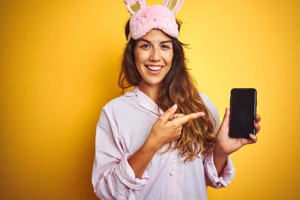 Młoda Kobieta Ubrana Piżamę Maskę Pomocą Smartfona Żółtym Białym Tle — Zdjęcie stockowe