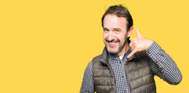 Orta yaş yakışıklı adamın gülümseyen kış Yelek giydiğini el ve parmak telefonda konuşmak ile telefon jest yapıyor. Kavramları iletişim.