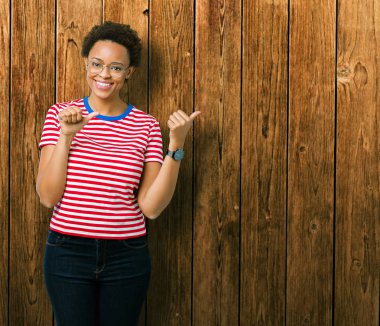 Güzel genç Afro-Amerikan kadın üzerinde gözlük takan izole arka plan emin gülümseyen arkasından el ve kadar başparmak ile işaret