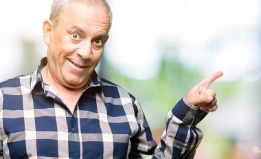 Yüzünde büyük bir gülümseme ile rahat gömlek giyen yakışıklı kıdemli adam, kamera bakarak yan el ve parmak ile işaret.