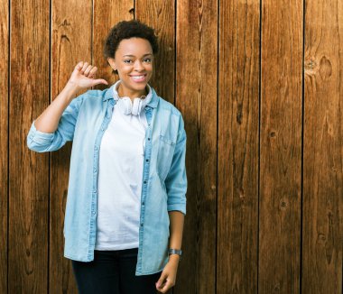 Yüzünde gülümseme ile kendinden emin görünüyorsun, kendini gururlu ve mutlu parmakları ile işaret izole arka plan üzerinde kulaklık giyen genç Afro-Amerikan kadın.