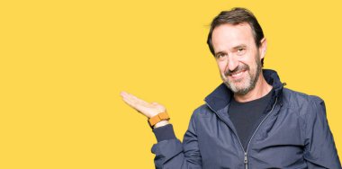 Orta yaş yakışıklı adam neşeli sunulması ve kameraya bakarak avucunun ile işaret gülümseyen bir ceket.