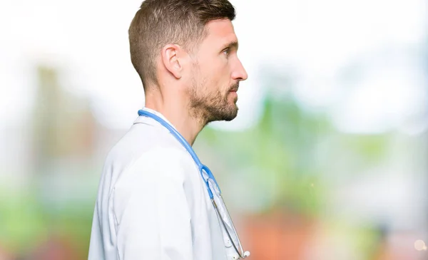 Handsome doctor man wearing medical uniform over isolated background looking to side, relax profile pose with natural face with confident smile.