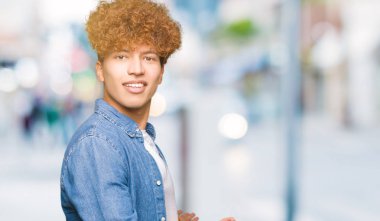 Genç yakışıklı adam ile afro saç giyen denim ceket açık el ile gülümseyen doğal girmek için davet