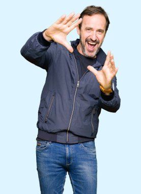 Orta yaş yakışıklı adam bir ceket giymiş el avuç içi ve parmaklar, kamera perspektifi kullanarak çerçeve yapıyor gülümseyen