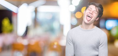 Genç yakışıklı adam giyen kış kazak dilini izole arka plan üzerinde out komik ifade ile mutlu. Duygu kavramı.