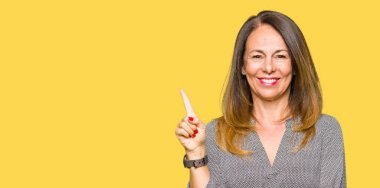 Kameraya bakarak yan el ve parmak ile işaret eden güzel orta yaş iş kadını yüzünde kocaman bir gülümseme ile.