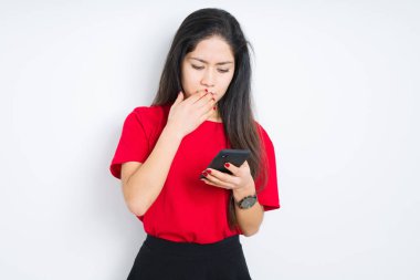 Genç esmer kadın izole arka plan kapağı ağız üzerinde akıllı telefon kullanarak el hata için utanç ile şok, korku ifadesi, sessizlik, gizli kavram korkmuş