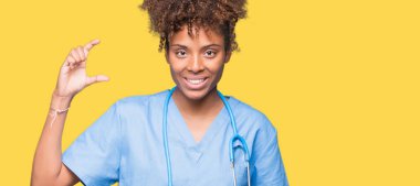 Genç Afro-Amerikan doktor kadın izole arka plan gülümseyen ve süre seyir ve kamera boyutu işaret parmaklarıyla yapıyor el ile kendine güvenen el hareketi yüzünden. Ölçü kavramı.