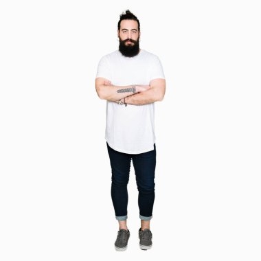 Uzun saç ve sakal yüz çapraz kolları olan casual beyaz t-shirt şüpheci ve sinir, onaylamayan ifade giyen genç hipster adam. Negatif kişi.