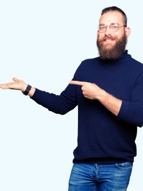 Gözlük ve hayrete ve el ile sunulması ve parmak ile işaret ederken kameraya gülümseyen boğazlı kazak giyen genç sarışın adam.