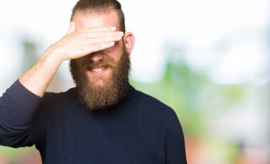 Gözlük ve gülümsüyor ve gözleri için sürpriz kapsayan yüz el ile gülüyor boğazlı kazak giyen genç sarışın adam. Kör kavramı.