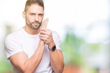 Yakışıklı adam açık havada arka plan üzerinde beyaz t-shirt giyen el hareketi ile sembolik silah holding, çekim silah öldürme oynarken, kızgın yüz