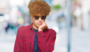 Yakışıklı genç afro saçlı stresli ve gergin elle çivi ısırma ağzına bakarak güneş gözlüğü takıyor. Anksiyete sorunu.