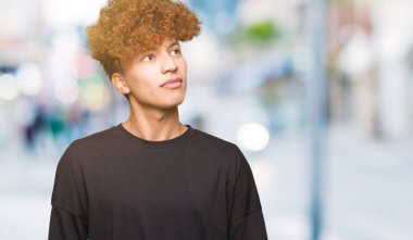Genç yakışıklı adam ile afro saç giyen siyah t-shirt gülümseyen görünümlü yan ve bakıyor Away düşünme.