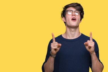 Yakışıklı delikanlı hayrete ve yukarıya bakıyor ve parmakları ile işaret ve silah kaldırdı sürpriz izole arka plan üzerinde gözlük.