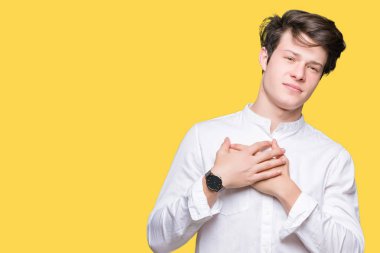 Genç yakışıklı iş adamı izole arka plan ile gülümseyen üzerinde kapalı gözler ve yüzünde minnettar jest ile göğüs üzerinde eller. Sağlık kavramı.