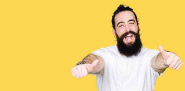 Uzun saç ve sakal casual beyaz t-shirt onaylama giyen genç hipster adamla el ile pozitif jest yapıyor gülümseyen ve başarı için mutlu Yaşasın. Kamera, kazanan jest arıyorsunuz.