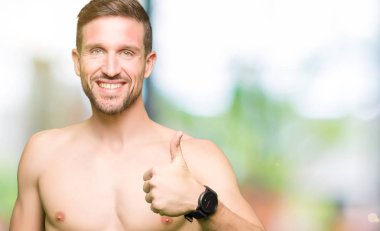 Gömleksiz yakışıklı gösteren çıplak göğüs hareketi el ile mutlu yaşasın yapıyor. Başarı gösteren kameraya bakarak ifade onaylama.