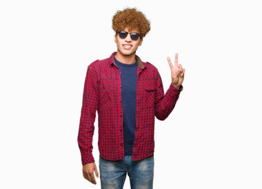 Yakışıklı genç afro saçlı gülen yüz zafer işareti yaparken kameraya göz kırpıyor ile gülümseyen güneş gözlüğü takıyor. İki numaralı.