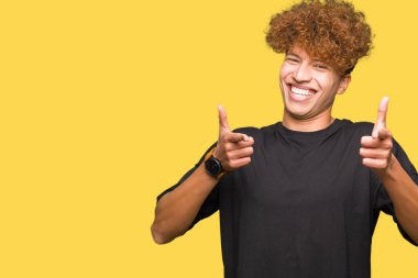 Genç yakışıklı adam ile afro saç giyen siyah t-shirt işaret parmaklar kamera ile mutlu ve komik yüz. İyi enerji ve Vibes.