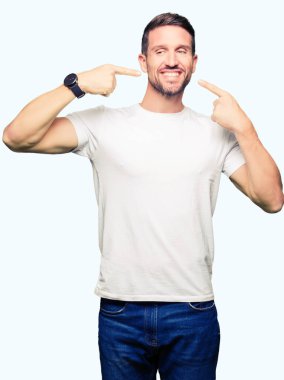 Yakışıklı adam kendinden emin gösterilen ve işaret parmakları diş ve ağız ile gülümseyen casual beyaz t-shirt giyiyor. Sağlık kavramı.