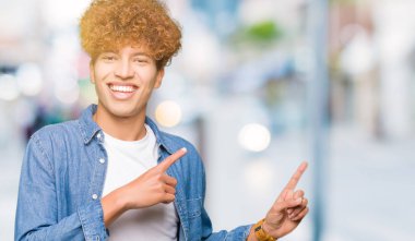 Gülümseyen ve iki elleri ve parmakları ile tarafına işaret kamera bakarak denim ceket giyen afro saçlı Genç yakışıklı adam.