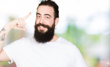 Uzun saç ve sakal casual beyaz t-shirt gülen bir parmak, harika bir fikir ya da düşünce, iyi hafıza ile baş gösteren giyen genç hipster adamla