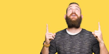 Casual kazak giyen genç sarışın adam hayret ve yukarıya bakıyor ve parmakları ile işaret ve silah kaldırdı şaşırttı.