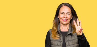 Kadar kış yelek gösterme ve işaret parmakları ile giyen güzel orta yaş kadın kendinden emin ve mutlu gülümseyerek iken üçüncü.