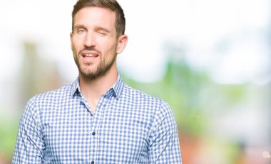 Yakışıklı iş adamı mavi gözlü seksi bir ifadeyle, neşeli ve mutlu yüzünü kameraya bakarak göz kırpıyor.