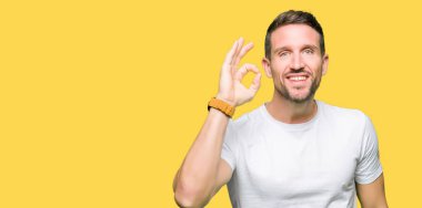 Yakışıklı adam el ve parmaklar ok işaretiyle yapıyor olumlu gülümseyen casual beyaz t-shirt giyiyor. Başarılı ifade.