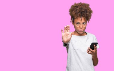 Açık eliyle dur işareti ile ciddi ve kendine güvenen ifade, savunma jest yapıyor izole arka plan üzerinde akıllı telefon kullanan genç Afro-Amerikan kadın