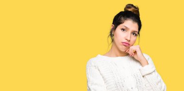 Çene düşünme hakkında soru, dalgın ifade üzerine el ile kış kazak giyen genç güzel kadın. Düşünceli yüzüyle gülümsüyor. Şüphe kavramı.