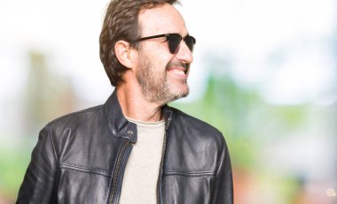 Güneş gözlüğü ve siyah deri ceket uzak tarafına gülümseme ile yüzünde, doğal ifade seyir giyen orta yaş yakışıklı adam. Kendine güvenen gülüyor.