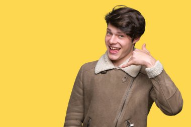 Genç yakışıklı adam giyen kış ceket yapmak gülümseyen izole arka plan üzerinde telefon hareketi ile el ve parmak telefonda konuşuyor gibi. Kavramları iletişim.