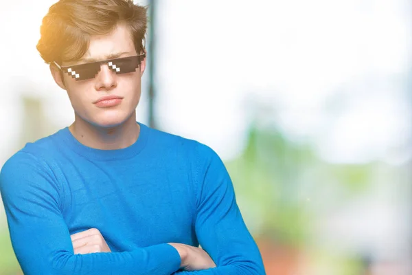 Young man wearing funny thug life glasses over isolated background skeptic and nervous, disapproving expression on face with crossed arms. Negative person.