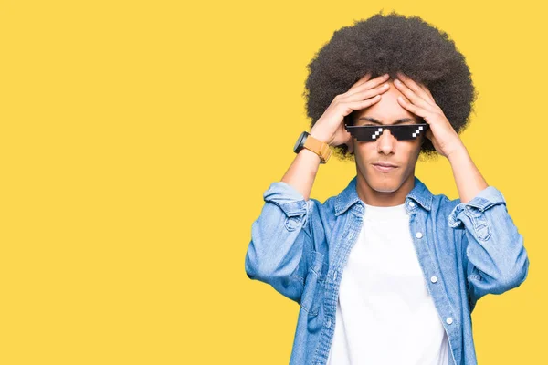 Young african american man with afro hair wearing thug life glasses suffering from headache desperate and stressed because pain and migraine. Hands on head.