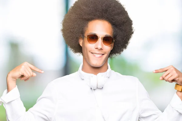 年轻的非洲裔美国男子与非洲头发戴着太阳镜和耳机看起来自信与微笑的脸 指着自己用手指骄傲和快乐 — 图库照片