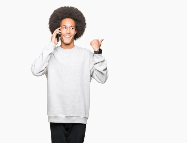 年轻的非洲裔美国男子与非洲头发交谈在智能手机指向和显示与大拇指到一边与快乐的脸微笑 — 图库照片