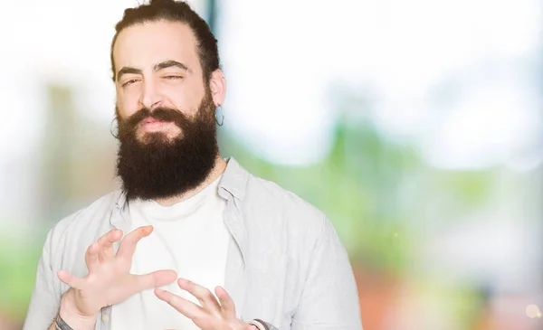 Young man with long hair, beard and earrings disgusted expression, displeased and fearful doing disgust face because aversion reaction. With hands raised. Annoying concept.