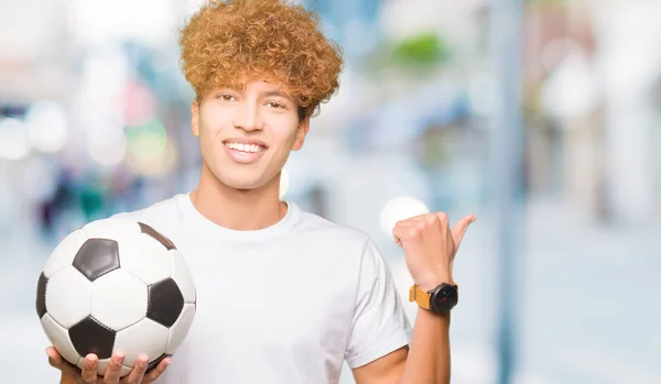 Joven Hombre Guapo Sosteniendo Pelota Fútbol Apuntando Mostrando Con Pulgar —  Fotos de Stock