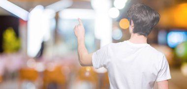 İzole arka planda rahat beyaz t-shirt giyen genç yakışıklı adam geriye parmak el ile işaret poz