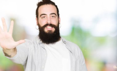 Uzun saç, sakal ve gösterilen ve parmakları ile işaret küpe ile genç adam kendinden emin ve mutlu gülümseyerek süre beş numara.