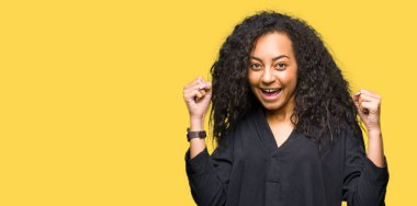 Kıvırcık saçlı genç güzel kız zarif elbise giyen sürpriz ve kollarını kaldırdı ve açık gözleri ile başarı için şaşırttı. Kazanan kavramı.