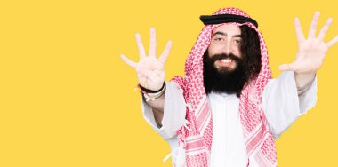 Arap iş adamı uzun saçlı gösterilen ve parmakları ile işaret geleneksel keffiyeh eşarp numara 9 kendinden emin ve mutlu gülümseyerek süre.