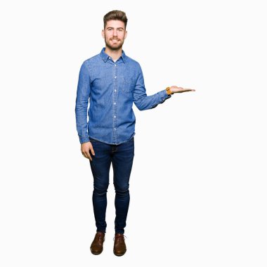 Genç yakışıklı sarışın adam neşeli sunulması ve kameraya bakarak avucunun ile işaret gülümseyen rahat kot gömlek giymiş.